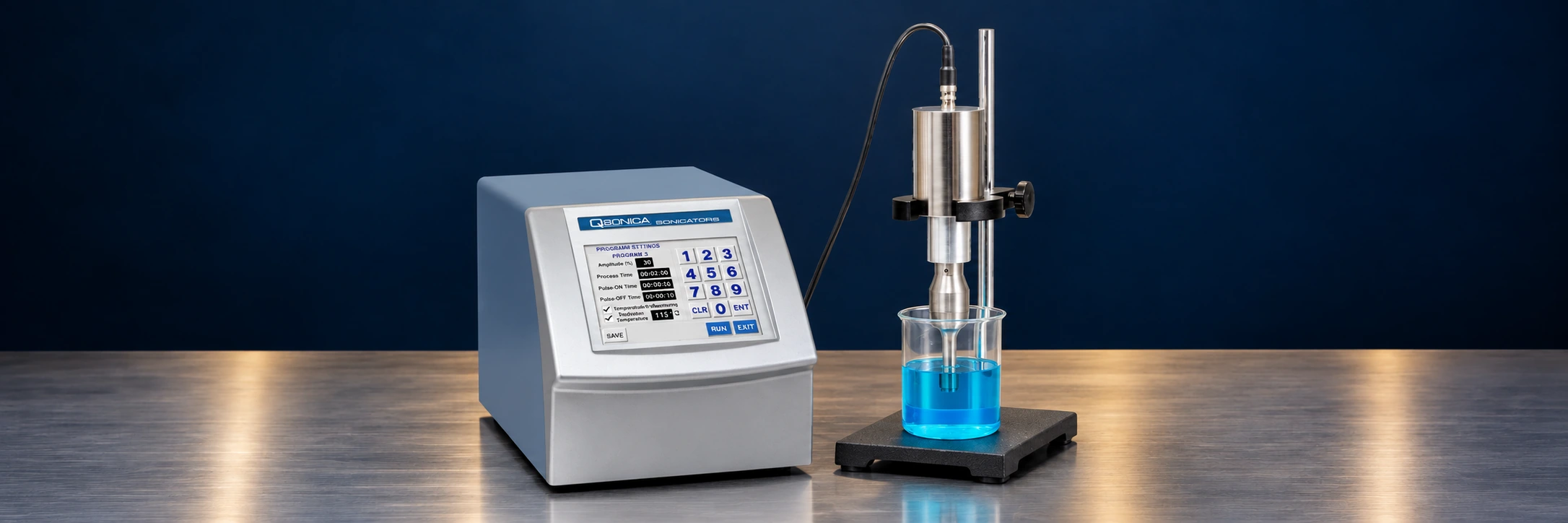 Ultrasonic processor, probe and sample vessel on a stainless steel bench against a navy background